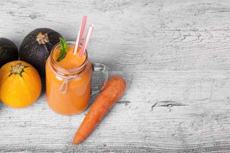 A view from above on a detox beverage next to a group of zucchinis and a carrot tube. A mason jar of orange yogurt and natural ingredients on a gray wooden background. Copy space. Health, diet conceptの写真素材
