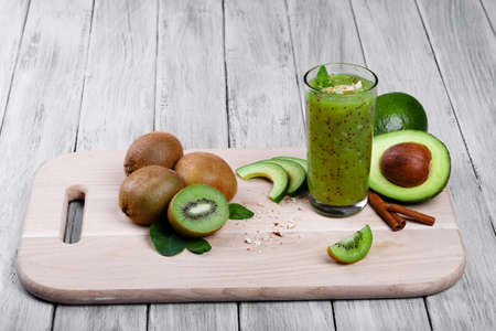 A colorful composition of organic, rustic fruits and vegetables on a cutting desk. A blended kiwi cocktail with peppermint and cinnamon. Cut avocados and heap of kiwis on a wooden background.の写真素材