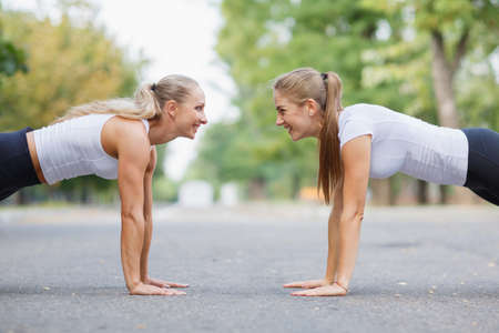 Fitness girls doing push-ups outdoors on a park background. Sporty girls. Workout concept. Copy...