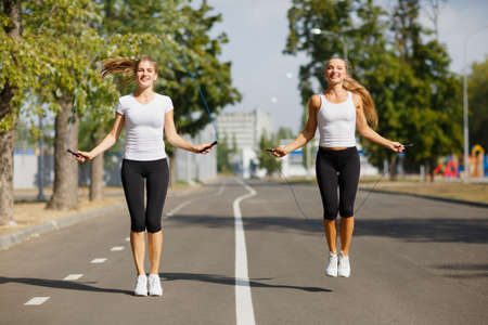 Gymnastics girls with jumping ropes on a park background. Sports friends. Active youth concept.の写真素材