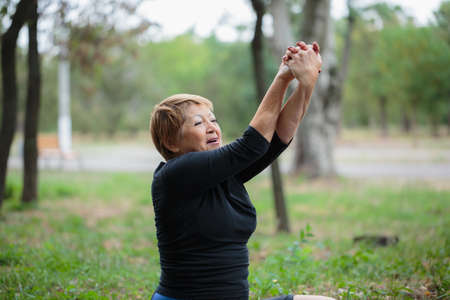 Nice elderly woman stretching and doing fitness on a garden background. Peaceful concept. Copy space.の写真素材