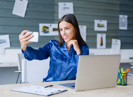 Young attractive woman working with laptop and posing on the camera in the office. Business concept.の写真素材