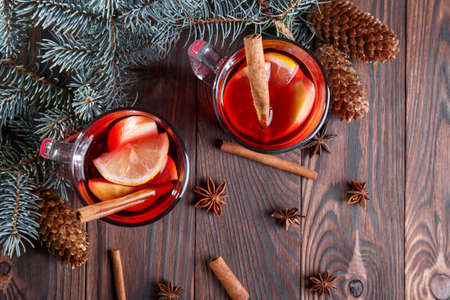 Two glasses full of red tea with lemons and cinnamon on a wooden table background. Warm, medical winter tea next to pine tree branch.の写真素材