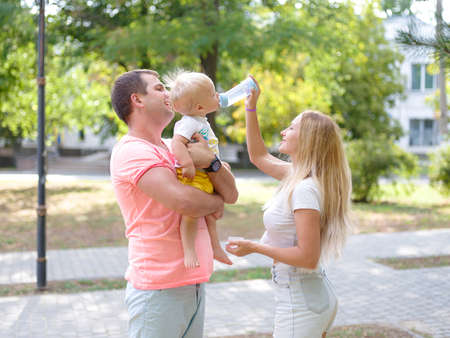 Dad holding baby boy and mother feeding him on a park background. Happy family. Baby food concept.の写真素材