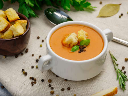 Pumpkin cream soup with carrots and bread in a white plate on light background. Food concept.の写真素材