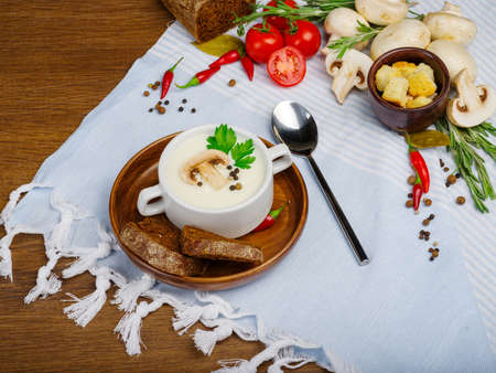 Mushroom cream soup with vegetables and bread in a white plate on a blue wooden table and blue litter. Food concept.の写真素材