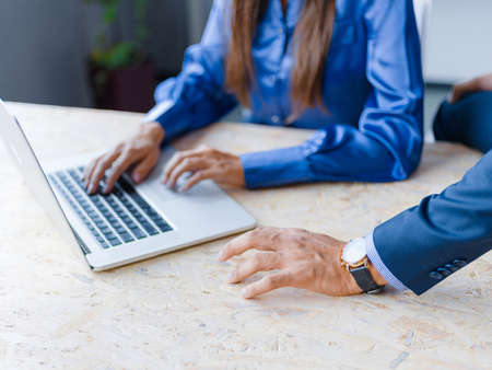 Handsome man and beautiful lady comunicate and working together on a project with computer. Grey wall on the background. Close-up of man hands. Business concept.の写真素材