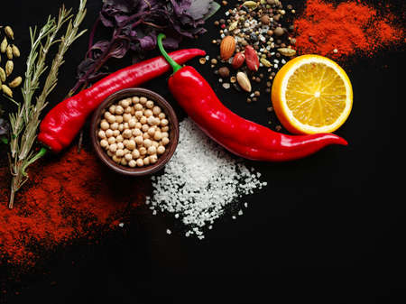 Two red pods of chili pepper, a slice of fresh orange, various fragrant species on a black background. Close-up of vegetables. Copy space.の写真素材