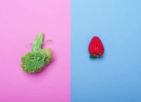 Fesh green broccoli lies on a pink background. Tasty ripe strawberry is depicted on a blue background. Copy space. Close-up of vegetables.の写真素材