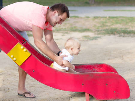 Happy dad playing with son on a slide on a park background. Family bonding concept. Copy space.の写真素材