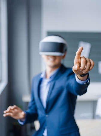 Funny handsome man wearing virtual reality glasses in modern interior design coworking studio. Smartphone using with VR goggles headset on blurred background. Business concept.の写真素材