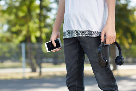 Mysterious guy with smartphone and headphones in hands on the park.の写真素材