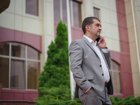 Businessman talking on a phone on the blurred office building background. Entrepreneur profession concept. Copy space.の写真素材