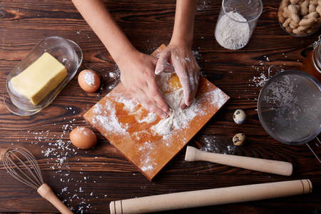 View from above of hands cracking and holding an egg on a baking table background. Desk with white flour and egg yolk for dough.の写真素材