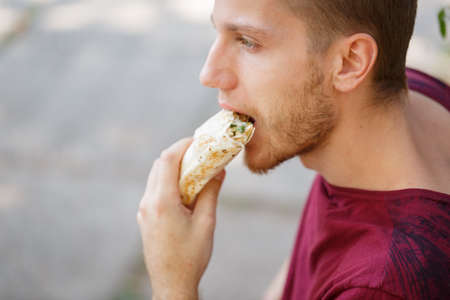 Young man with tasty shawarma outdoors.の写真素材