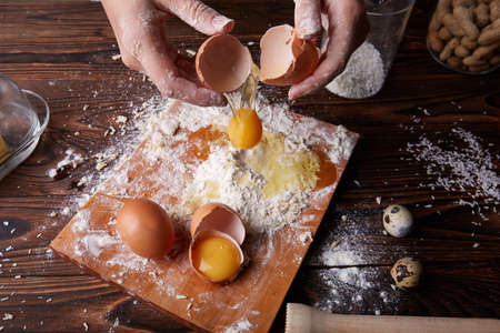 View from above of hands cracking and holding an egg on a baking table background. Desk with white flour and egg yolk for dough.の写真素材