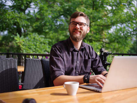 Goodly young man working on laptop while sitting outdoors . Business concept.