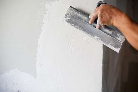 Construction worker with long trowel plastering a wall.