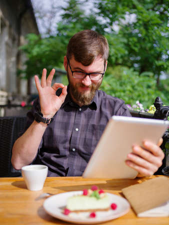 Goodly young man working on tablet while sitting outdoors . Business concept.