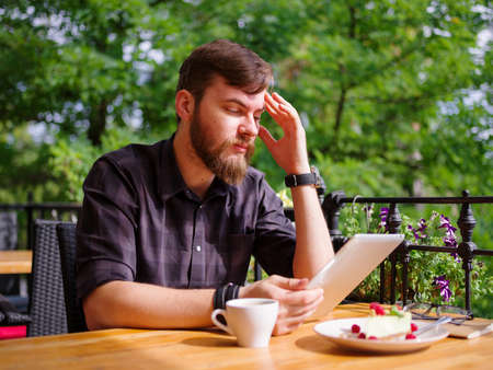 Goodly young man working on tablet while sitting outdoors . Business concept.の写真素材