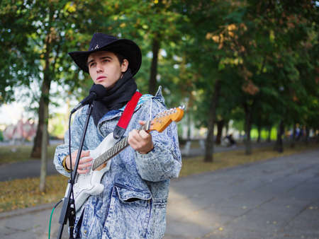 Young guy sings songs and plays guitar on a jeans jacket in a park on a natural background.の写真素材