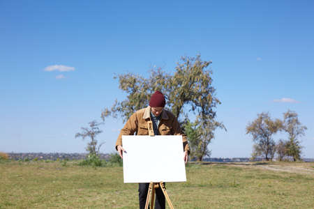 Young artist painting an autumn landscape on the nature background. Art concept.