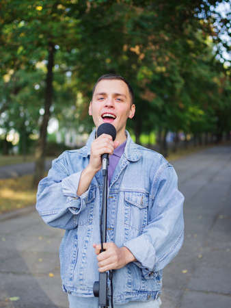 Young guy sings songs and plays guitar on a jeans jacket in a park on a natural background.の写真素材