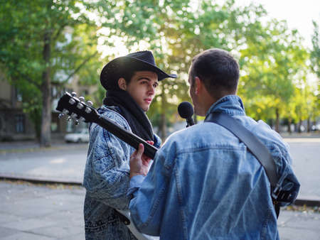 Happy young guys sings songs and plays guitar on a jeans jacket in a park on a natural background.の写真素材