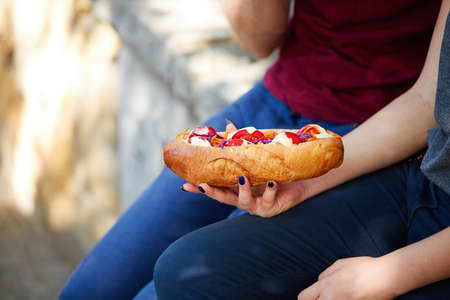 Young happy couple with tasting hotdog in the park.