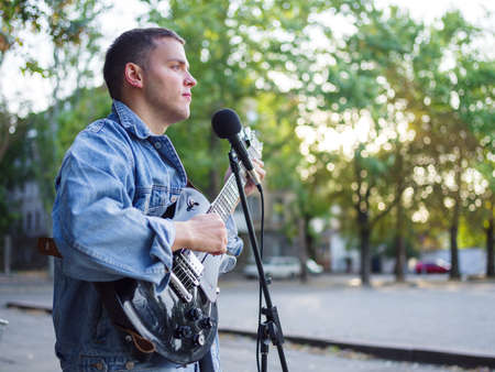 Young guy sings songs and plays guitar on a jeans jacket in a park on a natural background.の写真素材
