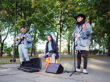 Young guy sings songs and plays guitar on a jeans jacket in a park on a natural background. Music...