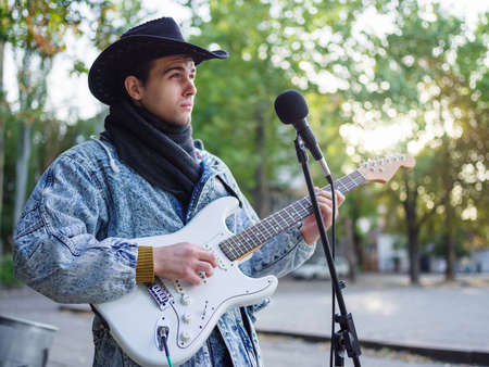 Young guy sings songs and plays guitar on a jeans jacket in a park on a natural background. Music...