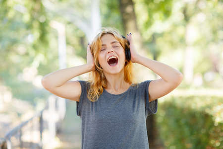 Modern carefree girl having fun with headphones on a park background. Student life concept. Copy...