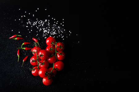 Top view of tomatoes and chili peppers on a black background. Spicy ketchup ingredients. Red...