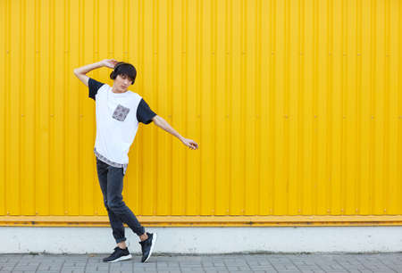 Casual student dancing to the music on a yellow wall background. Active lifestyle concept. Copy space.の写真素材