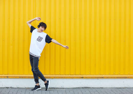 Casual student dancing to the music on a yellow wall background. Active lifestyle concept. Copy space.の写真素材