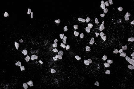 White, aromatic, therapeutic sea salt on a black stone background. Traditional condiments. Spilled mineral salt on a table.の写真素材