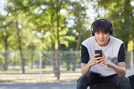 Young asian student with a new smartphone and headphones on a street background. Technology concept. Copy space.の写真素材