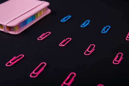 Close-up on a black background spread out pink and blue paper clips and a pink notebook.の写真素材