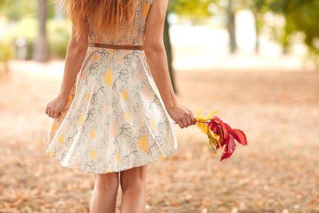 Close-up of a girl in a white dress which holds autumn leaves in hands.の写真素材
