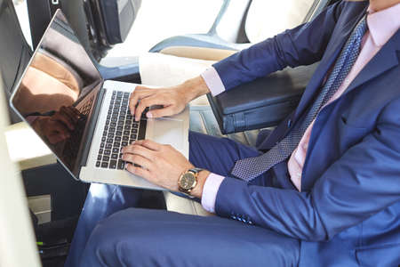 Close-up of a young businessman who uses a laptop to work in the backseat of a car.