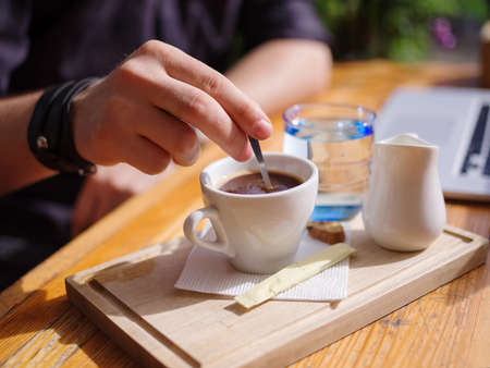 Close-up of a man stirs his coffee in a cafe in the fresh air.