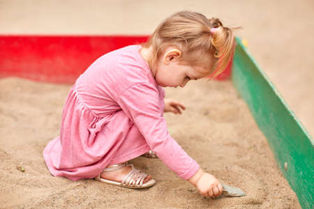 Little girl in a pink dress in a sandbox.の写真素材