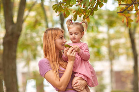 Young mother on a walk with daughter and leaf in hands.の写真素材