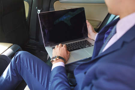 Young businessman using laptop in back seat of carの写真素材