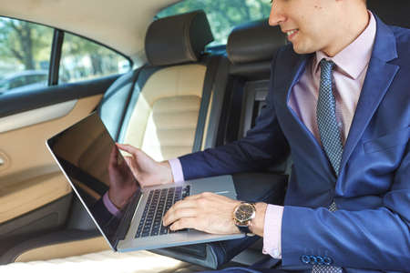 Young businessman using laptop in back seat of carの写真素材