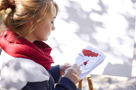 The female artist is painting a picture in the autumn park.の写真素材