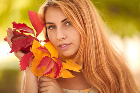 Girl in white dress with autumn leaves in handsの写真素材