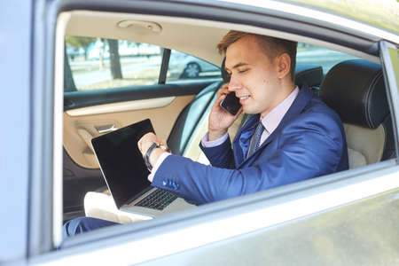 Confident businessman talking on mobile phone sitting in the back seat of a carの写真素材