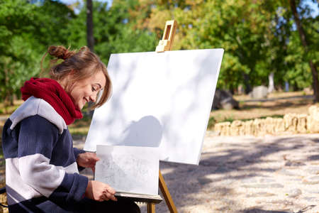 The female artist is painting a picture in the autumn park.の写真素材